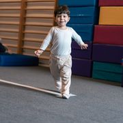 Çocuk zemindeki çizgi üzerinde yürüyor, arkasında İsveç merdiveni ve minder istifleri